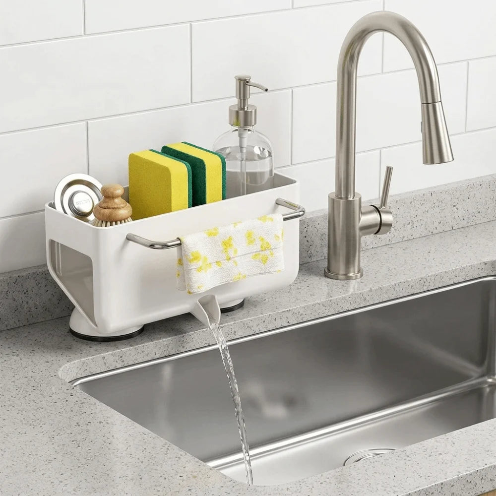 A white kitchen sink drain organizer with a hanging towel and sponge holder, shown installed on a speckled gray countertop next to a stainless steel sink and faucet.