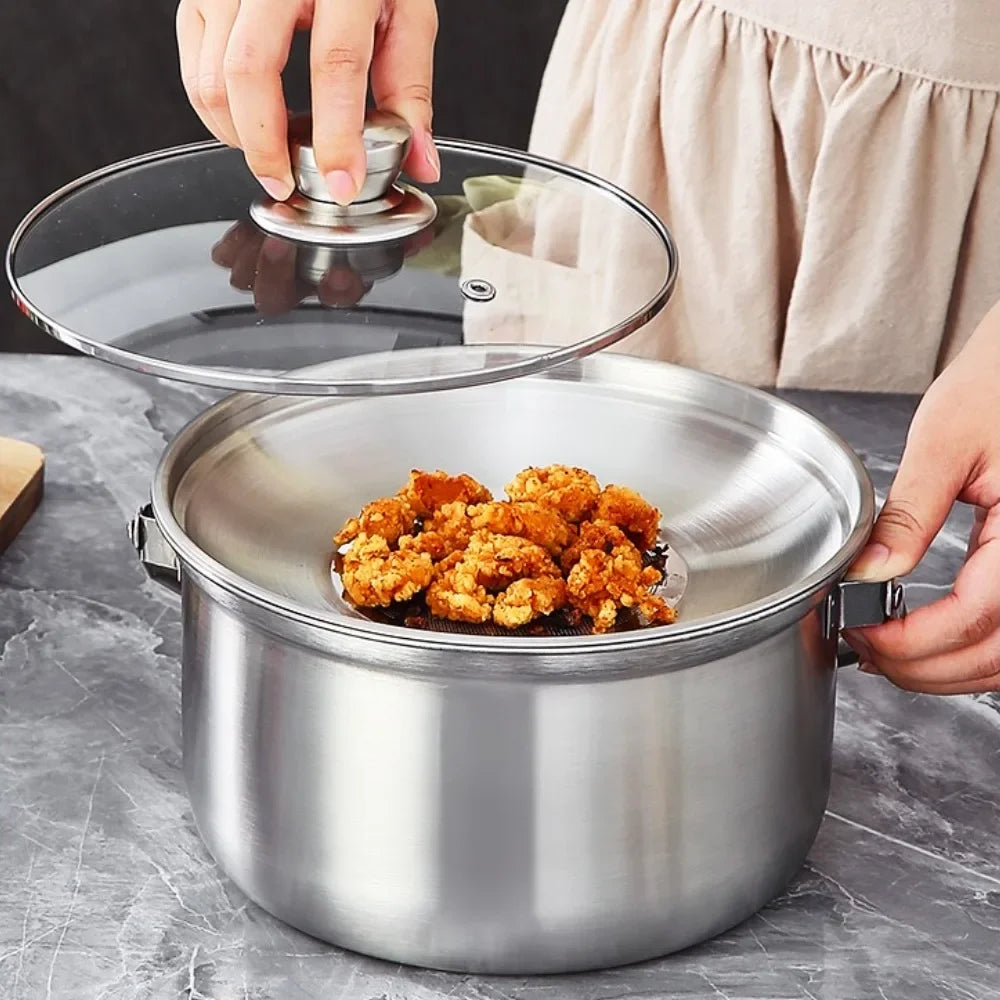 A stainless steel pot with a clear glass lid being lifted by hands, with fried food resting inside on a gray marble countertop.