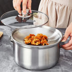 A stainless steel pot with a clear glass lid being lifted by hands, with fried food resting inside on a gray marble countertop.