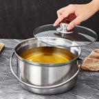 A stainless steel soup pot with a glass lid being lifted by a hand, showing a yellow soup inside, set on a gray marble countertop.