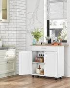 A white rolling kitchen cart with a light wood top stands in a bright kitchen. The cart has two front doors, one open to show shelves with jars and a small container, and is mounted on black caster wheels.