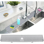 Gray kitchen sink mat on a kitchen counter with a window and plant in the background.