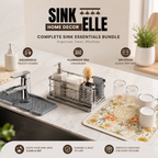 Sink Essentials Bundle set displayed on a kitchen sink counter, including a chrome faucet with a gray drain guard, a stainless steel FlowRack organizer, a Drystone quick-dry mat, soap dispenser, sponge, and glassware on a floral mat.