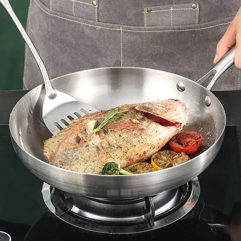 Stainless steel frying pan with meat and vegetables on a stove